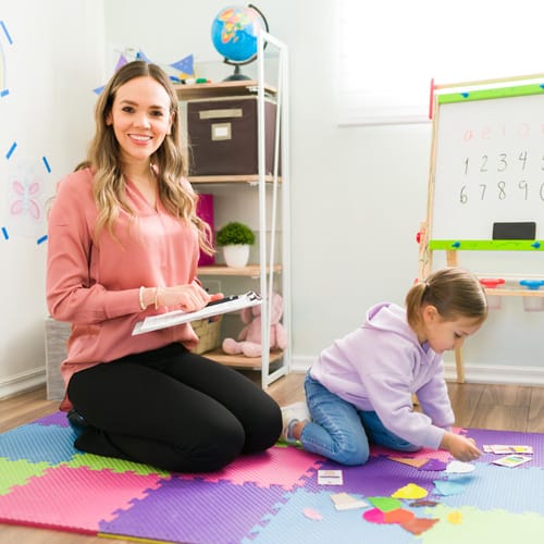 therapist on floor with child smiling at camera