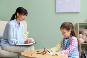 Woman watching a child draw during an autism assessment session, illustrating the need to prepare beforehand