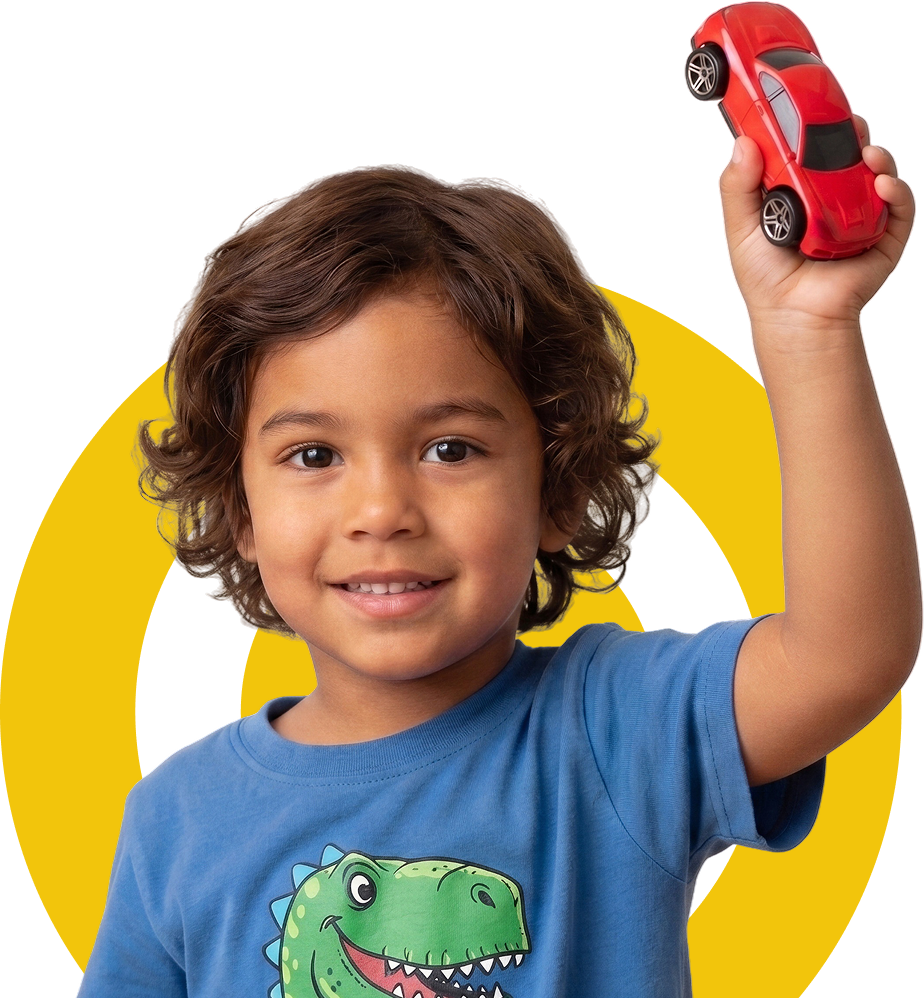 Young boy wearing a blue t-shirt with a dinosaur graphic, smiling while holding up a red toy car.
