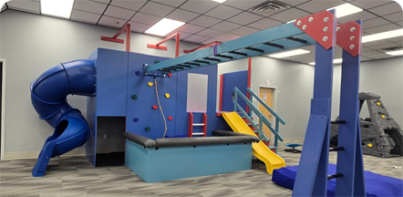 Indoor playground equipment featuring a blue enclosed slide, climbing wall, monkey bars, and a yellow slide.