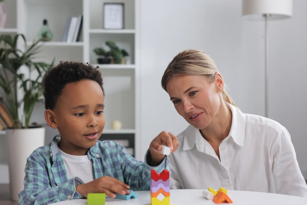 A therapist works with a young child during an ABA behavioral assessment, using colorful building blocks.
