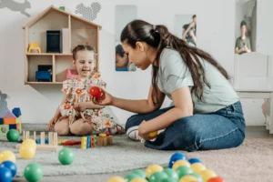ABA therapist showing girl with autism red ball while sitting on floor together during therapy.
