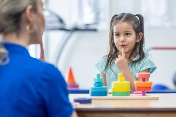 Child-working-with-therapist BCBA works with girl as she puts her fingers on her lips during an ABA exercise